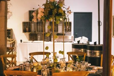Salle de réception avec tables rondes dressées, nappes blanches, chaises en bois et décoration florale.