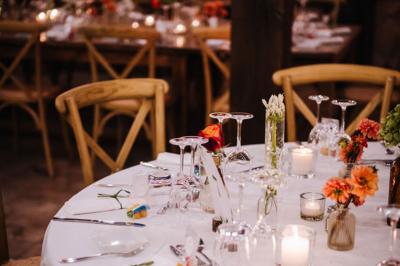Salle de réception avec tables rondes dressées, nappes blanches, chaises en bois et décoration florale.