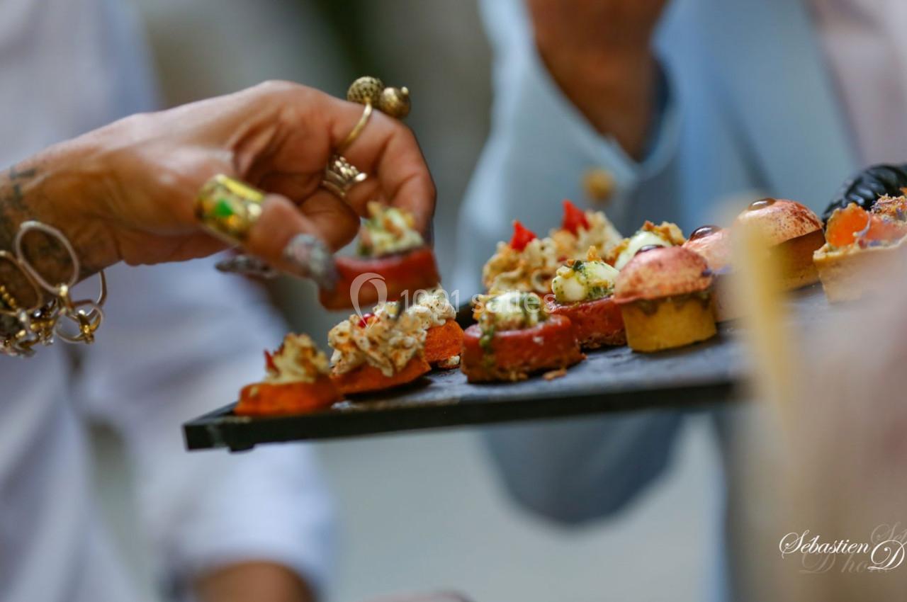 Des mains prennent des amuse-bouches variés sur un plateau noir lors d'un événement convivial.