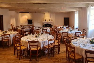 Salle de réception avec tables rondes dressées, nappes blanches, chaises en bois et décoration florale.