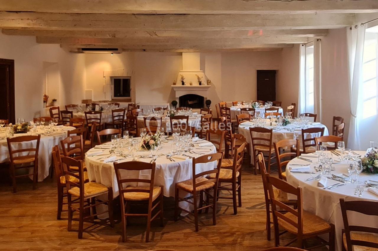 Salle de réception avec tables rondes dressées, nappes blanches, chaises en bois et décoration florale.