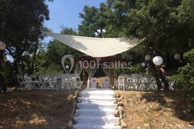 Un couple en tenue de mariage coupe une pièce montée décorée, devant un mur en pierre.