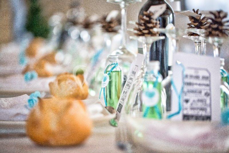 Table décorée avec des bouteilles miniatures, des pommes de pin et des pains individuels pour un repas festif.