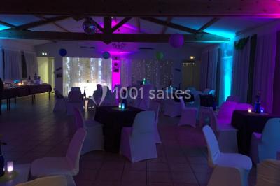 Un couple en tenue de mariage coupe une pièce montée décorée, devant un mur en pierre.