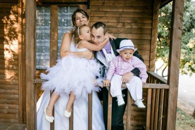 Un couple en tenue de mariage coupe une pièce montée décorée, devant un mur en pierre.