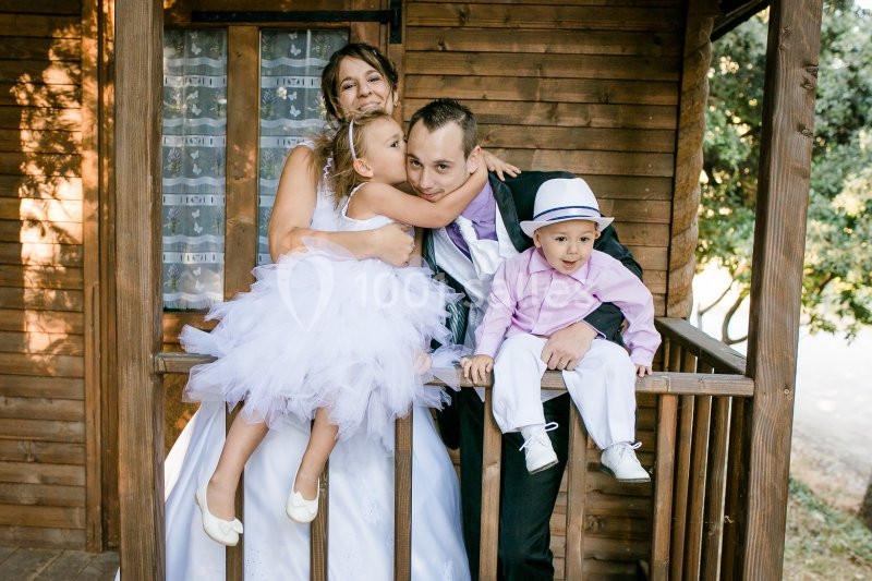 Une famille souriante posant sur le balcon en bois d'une maison, avec deux enfants en tenue élégante.
