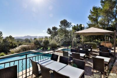 Un couple en tenue de mariage coupe une pièce montée décorée, devant un mur en pierre.
