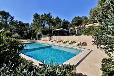 Un couple en tenue de mariage coupe une pièce montée décorée, devant un mur en pierre.