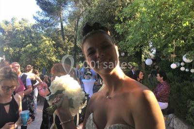 Un couple en tenue de mariage coupe une pièce montée décorée, devant un mur en pierre.