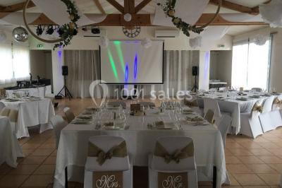 Un couple en tenue de mariage coupe une pièce montée décorée, devant un mur en pierre.