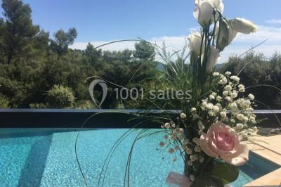Un couple en tenue de mariage coupe une pièce montée décorée, devant un mur en pierre.
