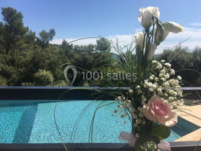 Bouquet de fleurs blanches et roses posé près d'une piscine avec vue sur des arbres et un ciel dégagé.