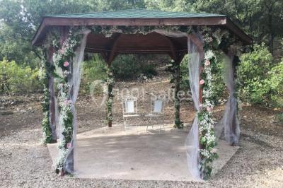 Un couple en tenue de mariage coupe une pièce montée décorée, devant un mur en pierre.