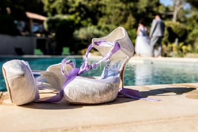 Un couple en tenue de mariage coupe une pièce montée décorée, devant un mur en pierre.