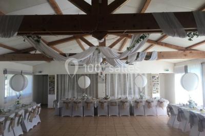 Un couple en tenue de mariage coupe une pièce montée décorée, devant un mur en pierre.