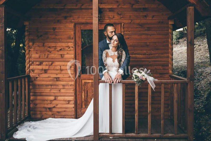 Un couple en tenue de mariage pose sur la terrasse en bois d'une petite cabane entourée de nature.