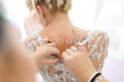 Un couple en tenue de mariage coupe une pièce montée décorée, devant un mur en pierre.
