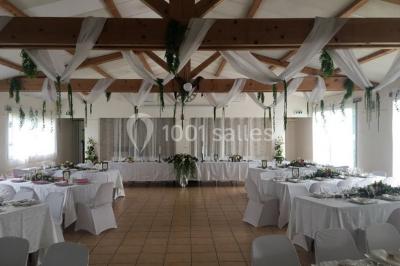 Un couple en tenue de mariage coupe une pièce montée décorée, devant un mur en pierre.