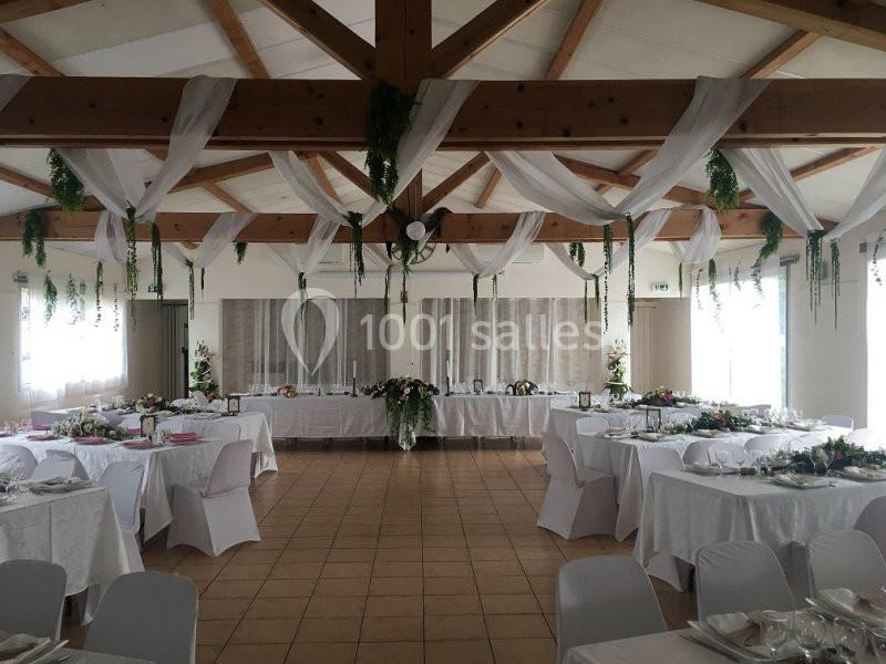 Salle de réception décorée avec des nappes blanches, des guirlandes végétales suspendues et des tables dressées.