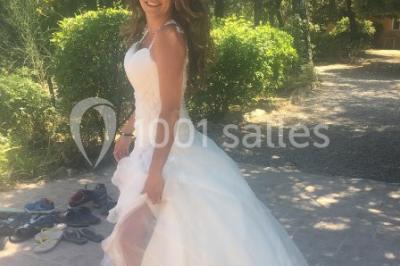 Un couple en tenue de mariage coupe une pièce montée décorée, devant un mur en pierre.