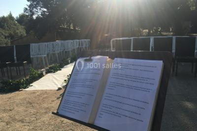 Un couple en tenue de mariage coupe une pièce montée décorée, devant un mur en pierre.
