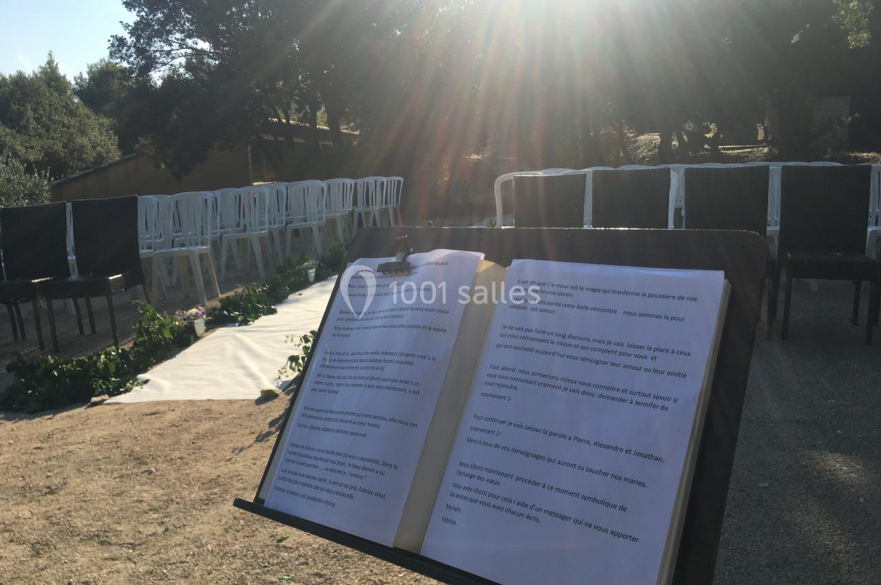 Livre ouvert sur un pupitre en plein air, devant des chaises disposées pour un événement sous un soleil éclatant.