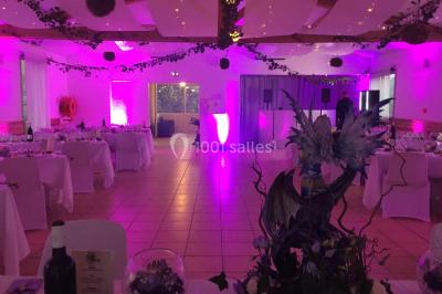 Un couple en tenue de mariage coupe une pièce montée décorée, devant un mur en pierre.