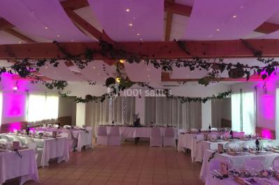 Un couple en tenue de mariage coupe une pièce montée décorée, devant un mur en pierre.