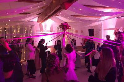 Un couple en tenue de mariage coupe une pièce montée décorée, devant un mur en pierre.