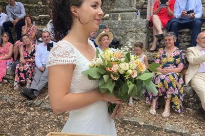 Un couple en tenue de mariage coupe une pièce montée décorée, devant un mur en pierre.