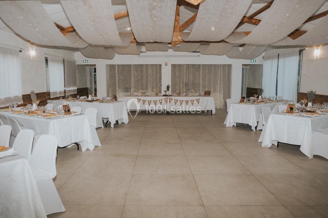 Salle de réception décorée avec des tables dressées, nappes blanches et guirlandes suspendues au plafond.