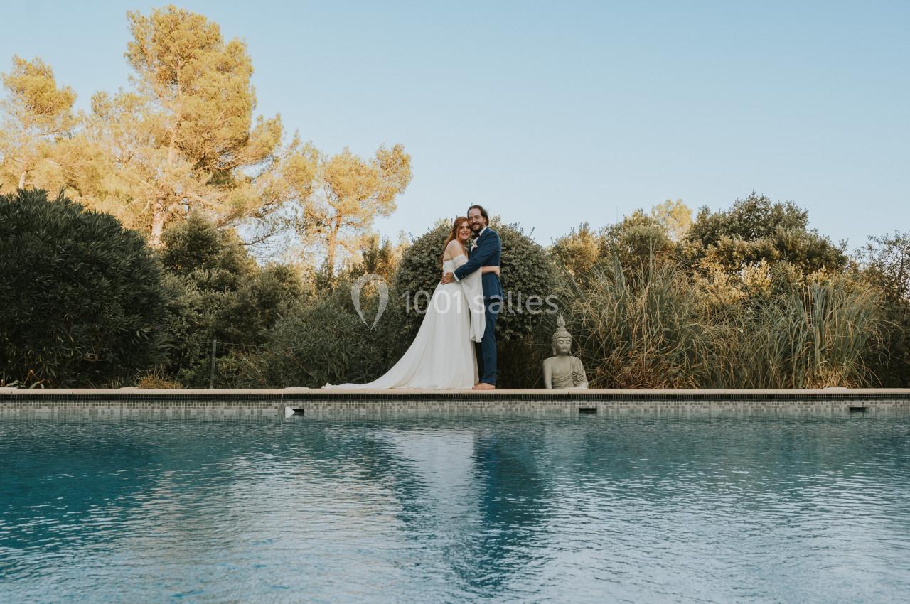 Un couple debout sur le bord d'une piscine, entouré de végétation et d'une statue de Bouddha.