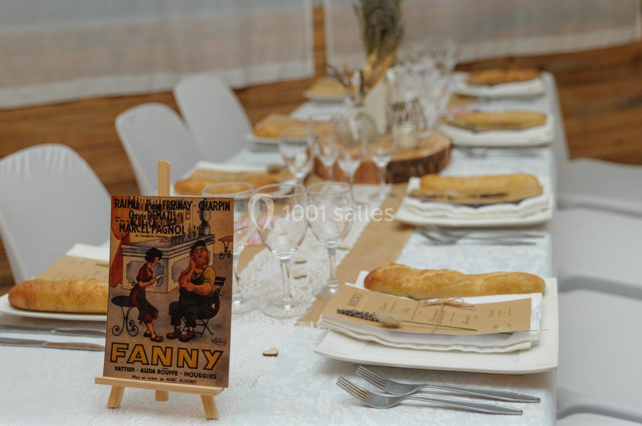 Table de réception décorée avec des assiettes, des verres, des baguettes de pain et une affiche rétro sur un chevalet.
