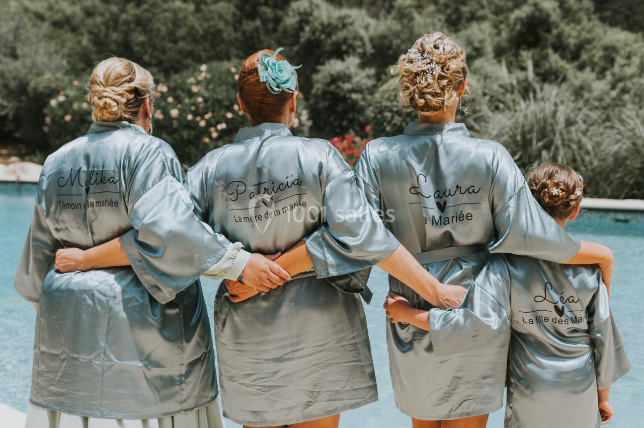 Quatre femmes en peignoirs satinés personnalisés, de dos, devant une piscine dans un cadre extérieur verdoyant.