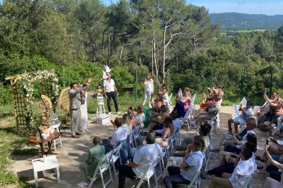 Un couple en tenue de mariage coupe une pièce montée décorée, devant un mur en pierre.