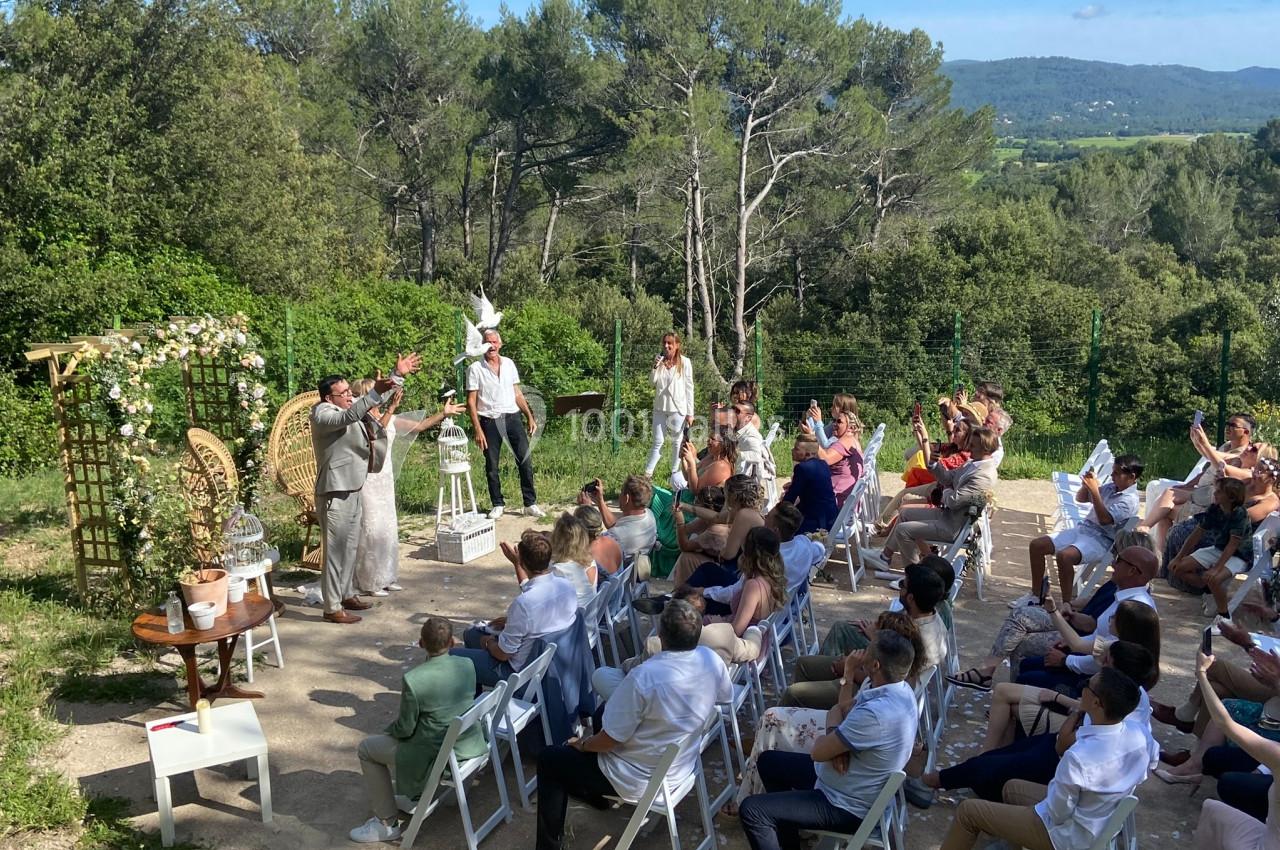 Cérémonie en plein air avec des invités assis, un officiant et un couple debout, entourés de végétation.