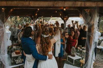 Un couple en tenue de mariage coupe une pièce montée décorée, devant un mur en pierre.