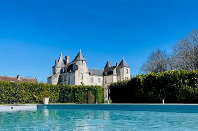 Miniature Location salle Marçay (Indre-et-Loire) - Château de Marcay #8 Chambre avec poutres apparentes, lit double, canapé beige, table basse en verre et murs décorés de papier peint.