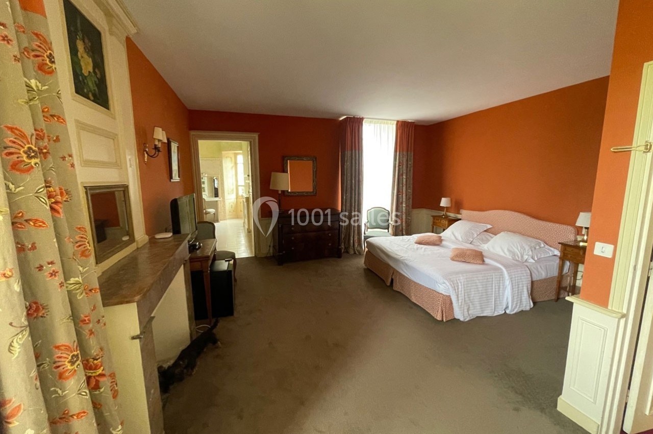 Chambre spacieuse avec murs orange, lit double, mobilier en bois, télévision et grande fenêtre avec rideaux.