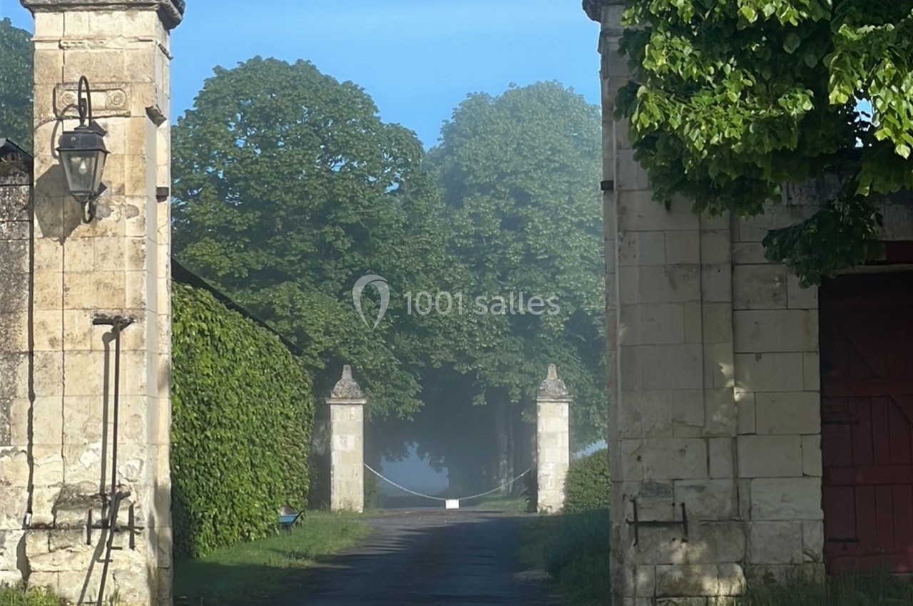 Entrée d'une propriété avec un portail en pierre, une allée bordée d'arbres et une légère brume matinale.