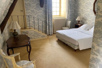 Miniature Location salle Marçay (Indre-et-Loire) - Château de Marcay #41 Chambre avec poutres apparentes, lit double, canapé beige, table basse en verre et murs décorés de papier peint.