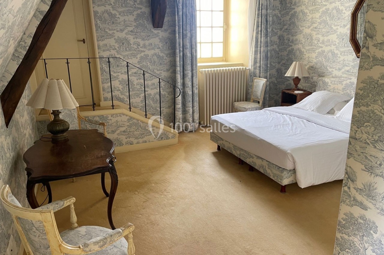 Chambre lumineuse avec lit double, mobilier classique en bois, murs et rideaux à motifs, et fenêtre donnant sur l'extérieur.