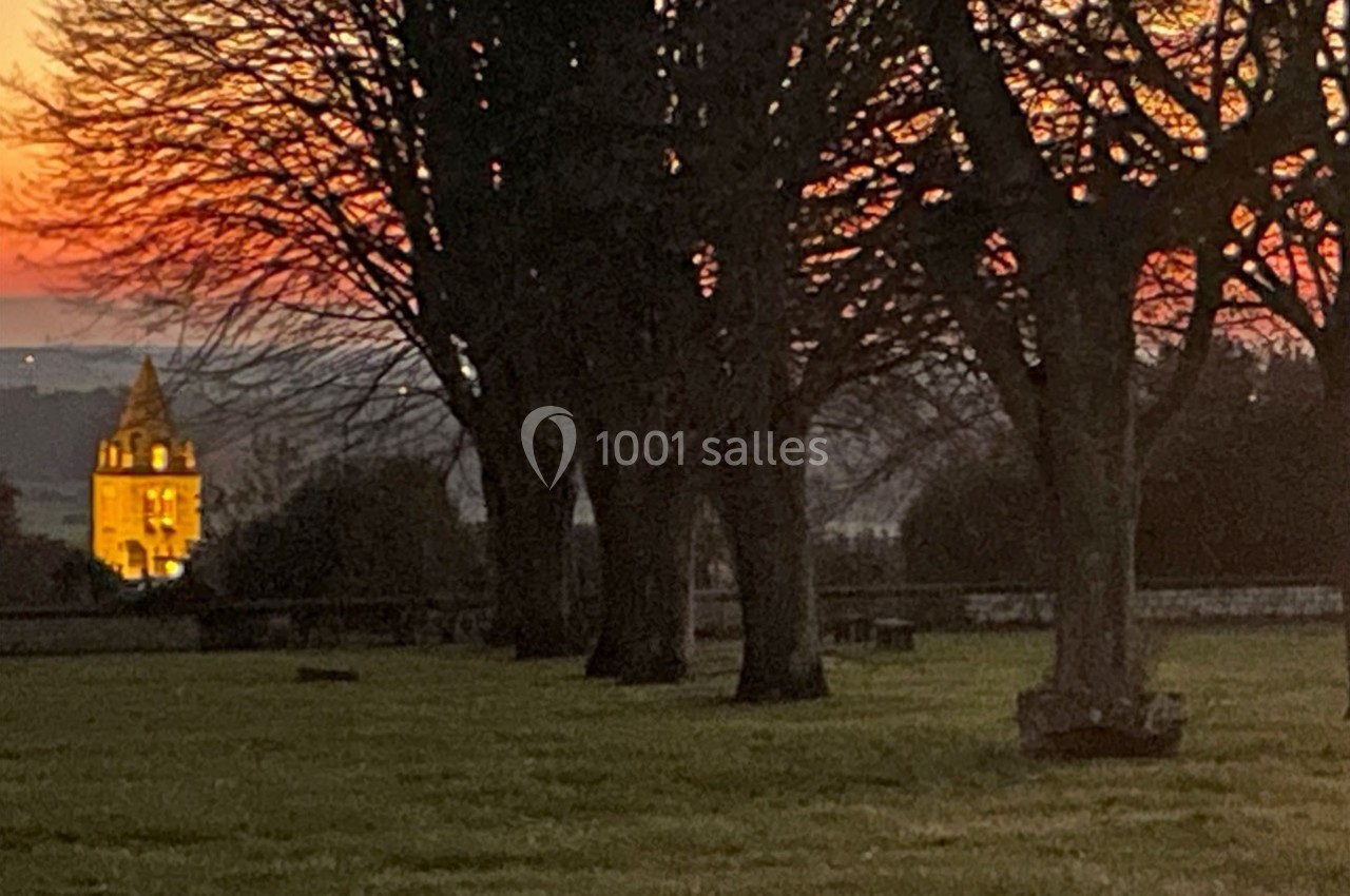 Clocher illuminé au crépuscule, entouré d'arbres dénudés et d'une pelouse verdoyante.