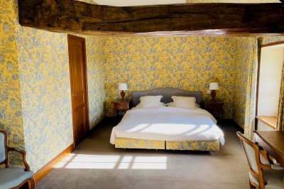 Miniature Location salle Marçay (Indre-et-Loire) - Château de Marcay #60 Chambre avec poutres apparentes, lit double, canapé beige, table basse en verre et murs décorés de papier peint.