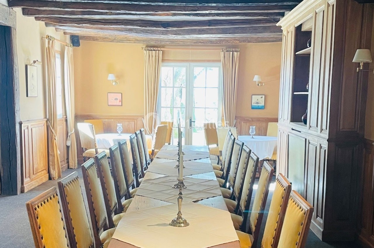 Salle à manger lumineuse avec une grande table en bois, chaises rembourrées et fenêtres donnant sur un jardin.