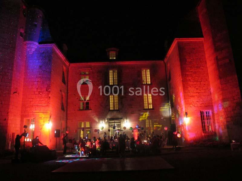 Façade d'un château éclairée par des lumières colorées, avec des personnes rassemblées dans la cour de nuit.
