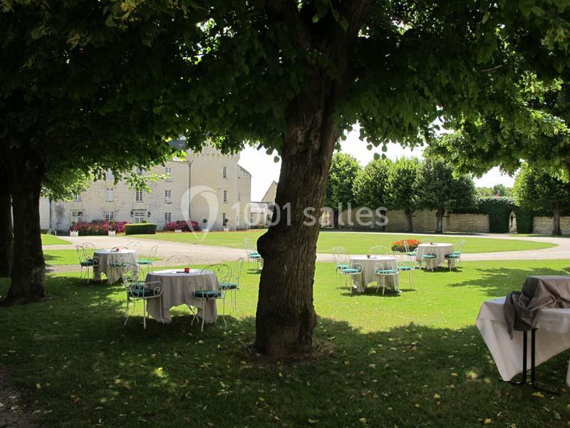 Tables et chaises disposées sur une pelouse ombragée, près d'un bâtiment en pierre, par une journée ensoleillée.