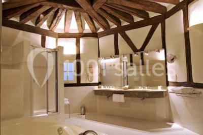 Miniature Location salle Marçay (Indre-et-Loire) - Château de Marcay #17 Chambre avec poutres apparentes, lit double, canapé beige, table basse en verre et murs décorés de papier peint.