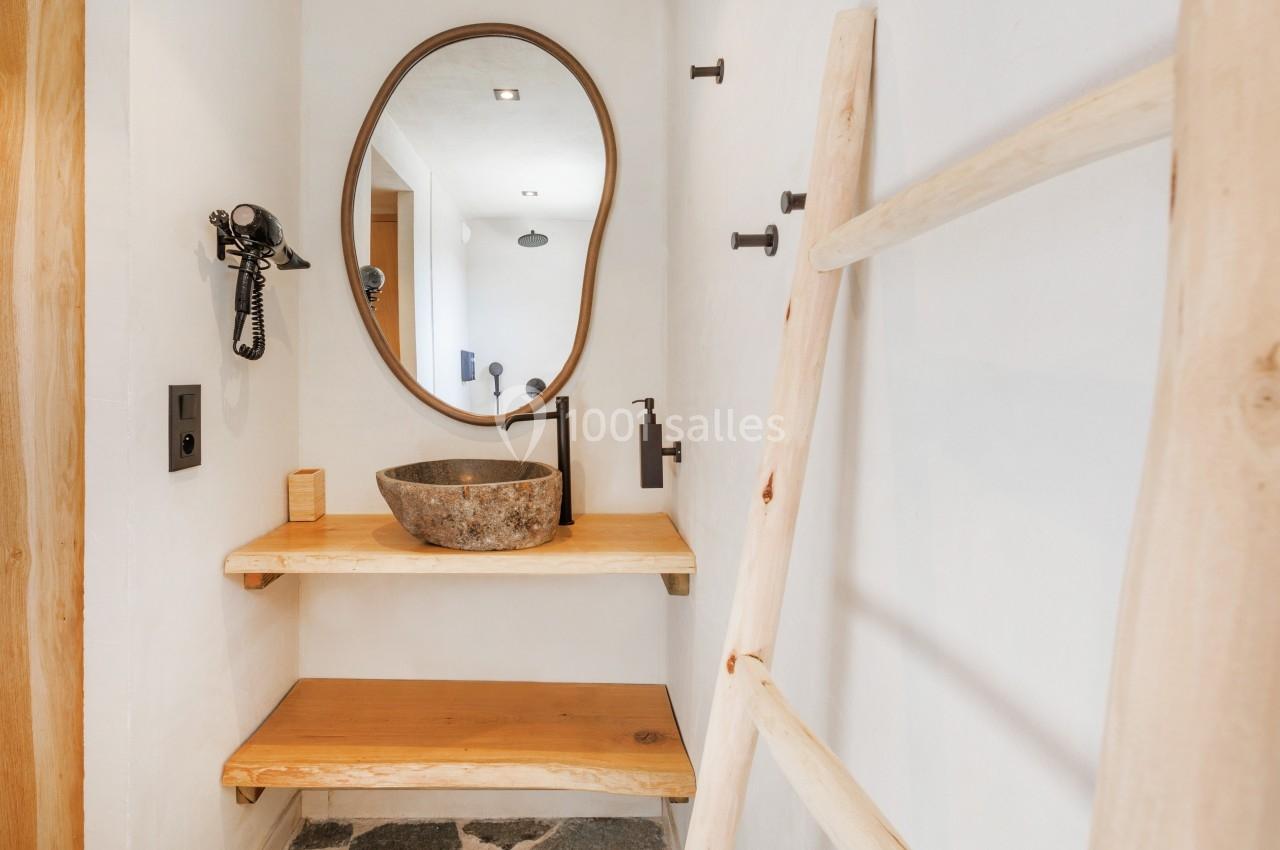 Petit espace de salle de bain avec miroir ovale, vasque en pierre, étagères en bois et échelle décorative.