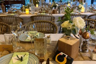 Table dressée avec assiettes en céramique, serviettes vertes pliées, couverts dorés, verres et décoration florale blanche.